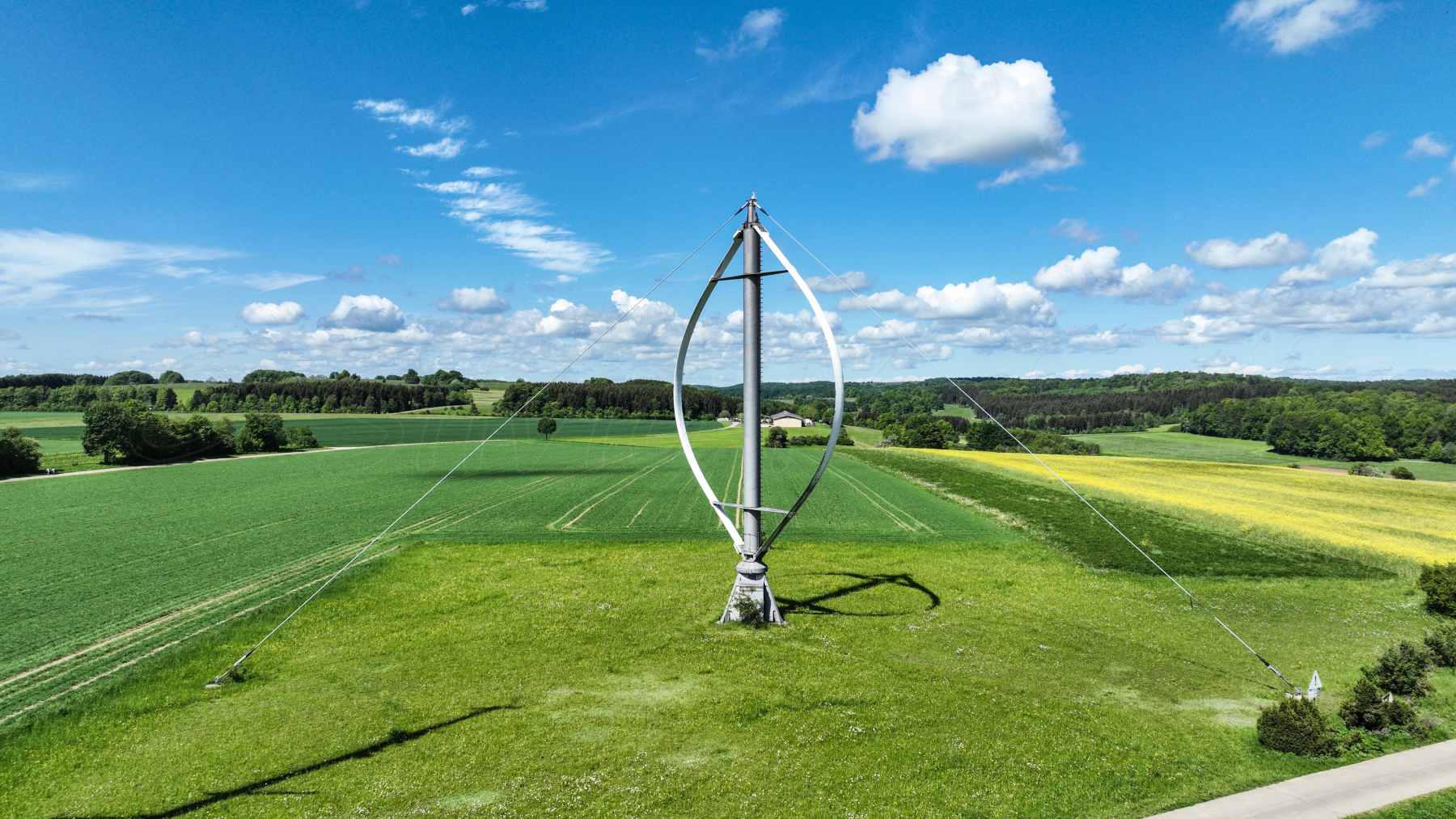 An egg-shaped vertical-axis wind turbine in a green field.