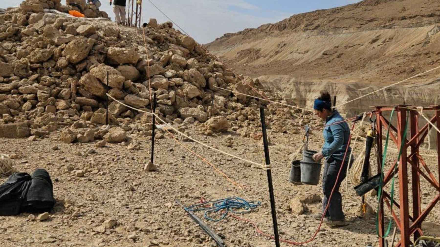 Archaeologist carrying a bucket beside rubble at the 2,200-year-old stone pyramid dig near Nahal Zohar, Judean Desert.