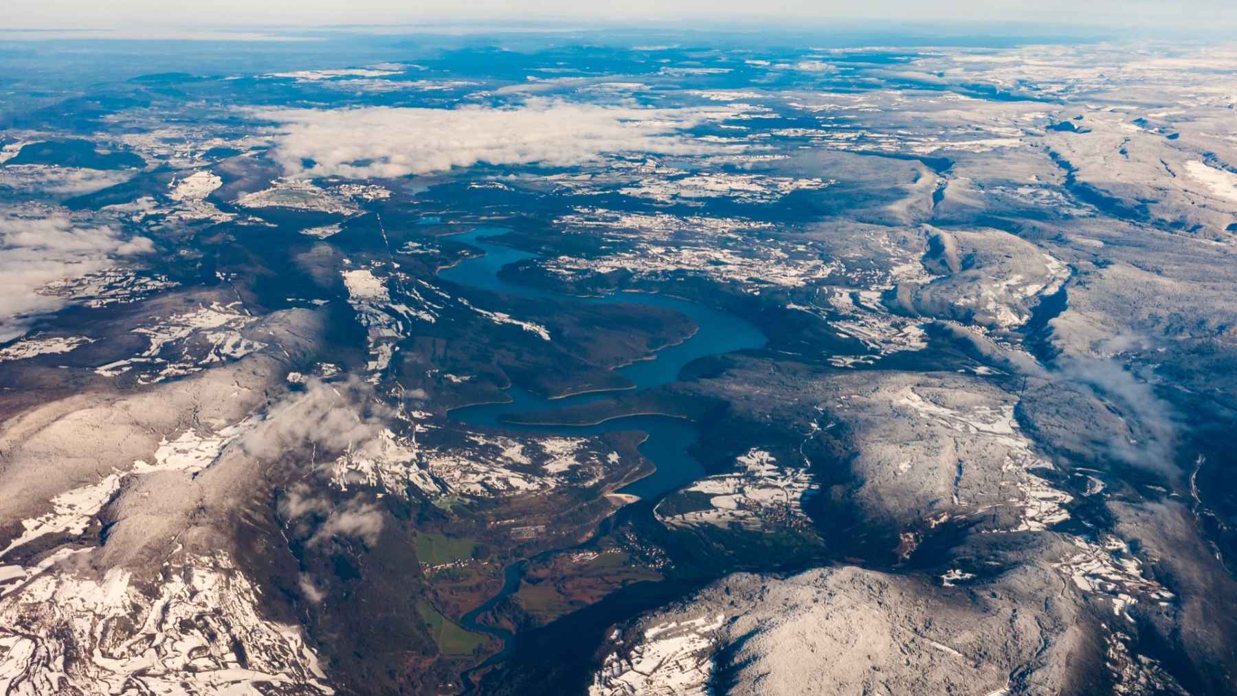 Vista aérea de montañas nevadas y un río/embalse serpenteante, imagen de apoyo sobre fenómenos extremos detectados por satélite.