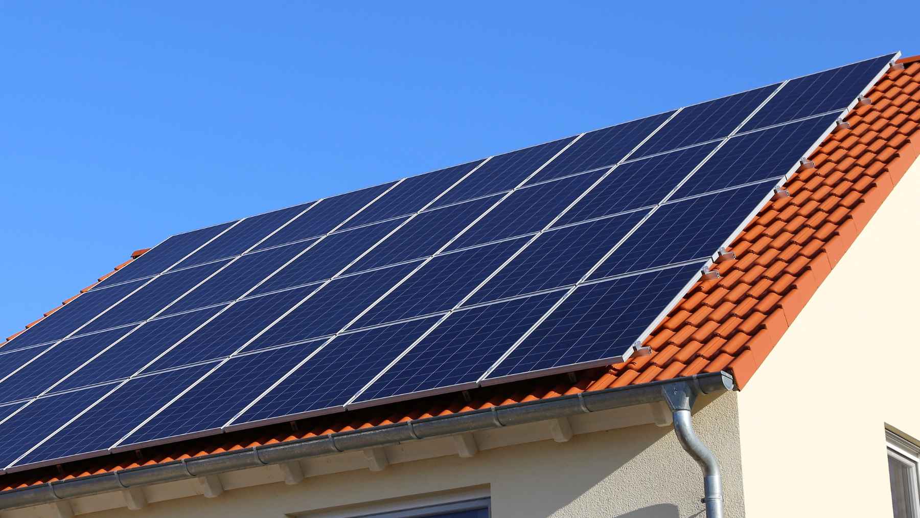 Paneles solares en el tejado de una vivienda con tejas, bajo cielo azul