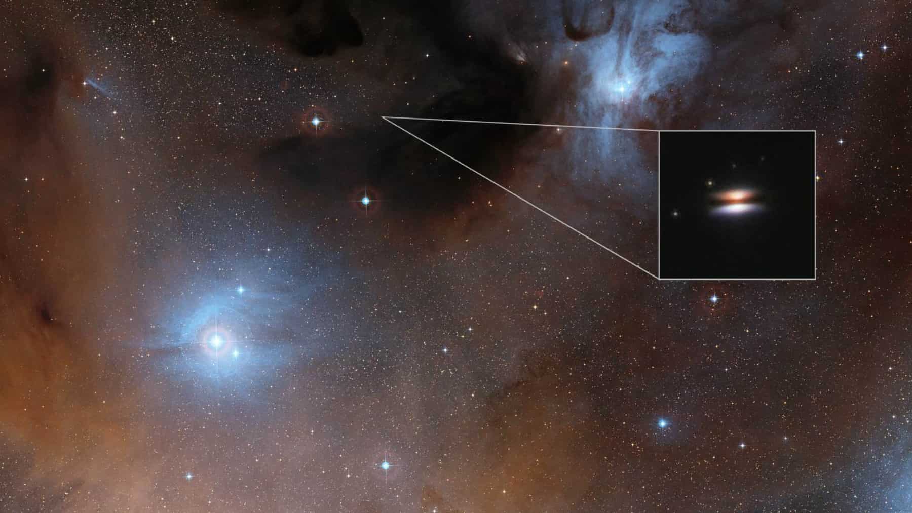 Campo estelar con nebulosa azul y nubes de polvo oscuro; un recuadro resalta una galaxia espiral vista de canto al fondo.