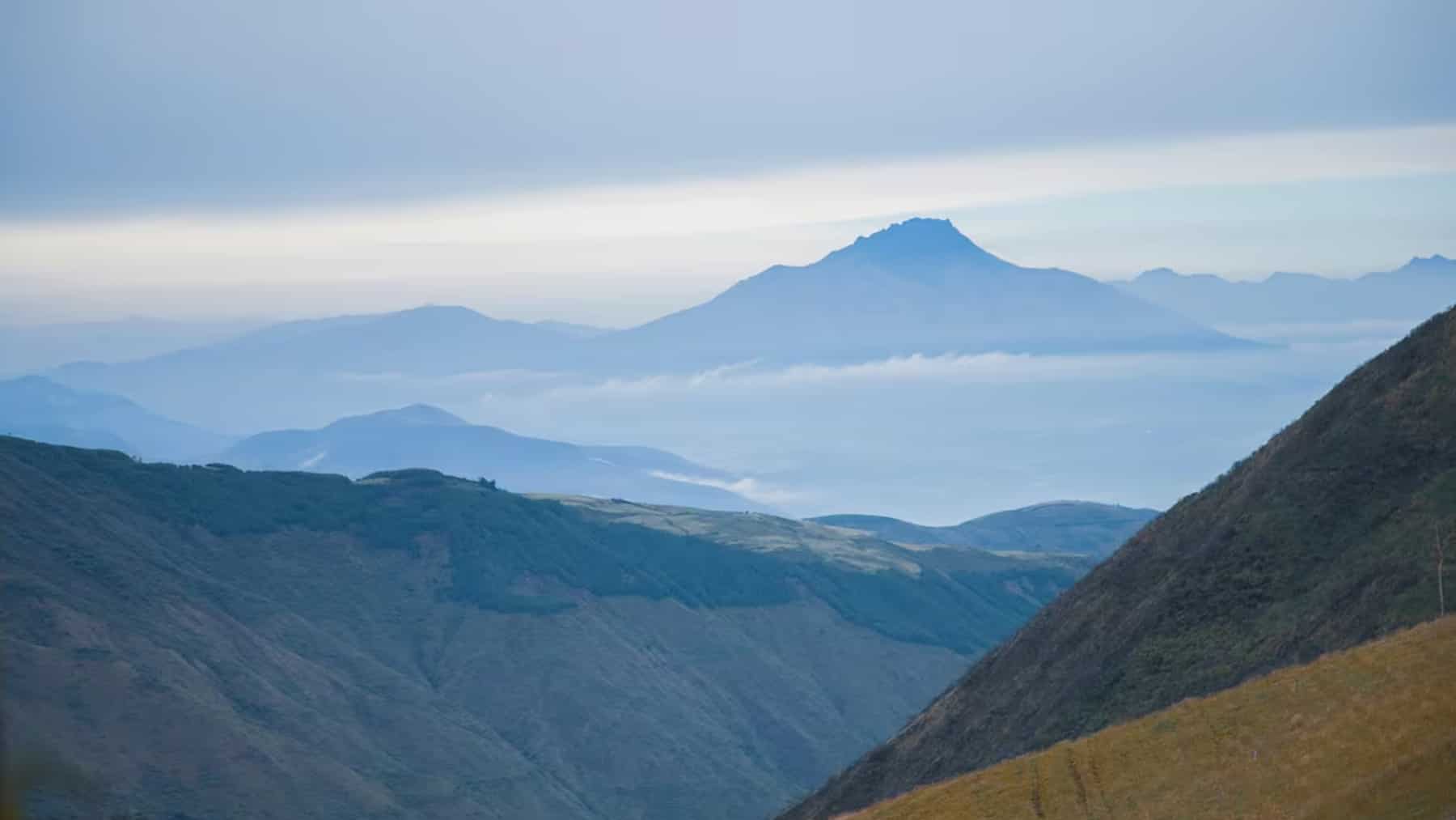 Vista panorámica de montañas en Carchi con capas de cordillera y un pico al fondo entre bruma y cielo nublado.
