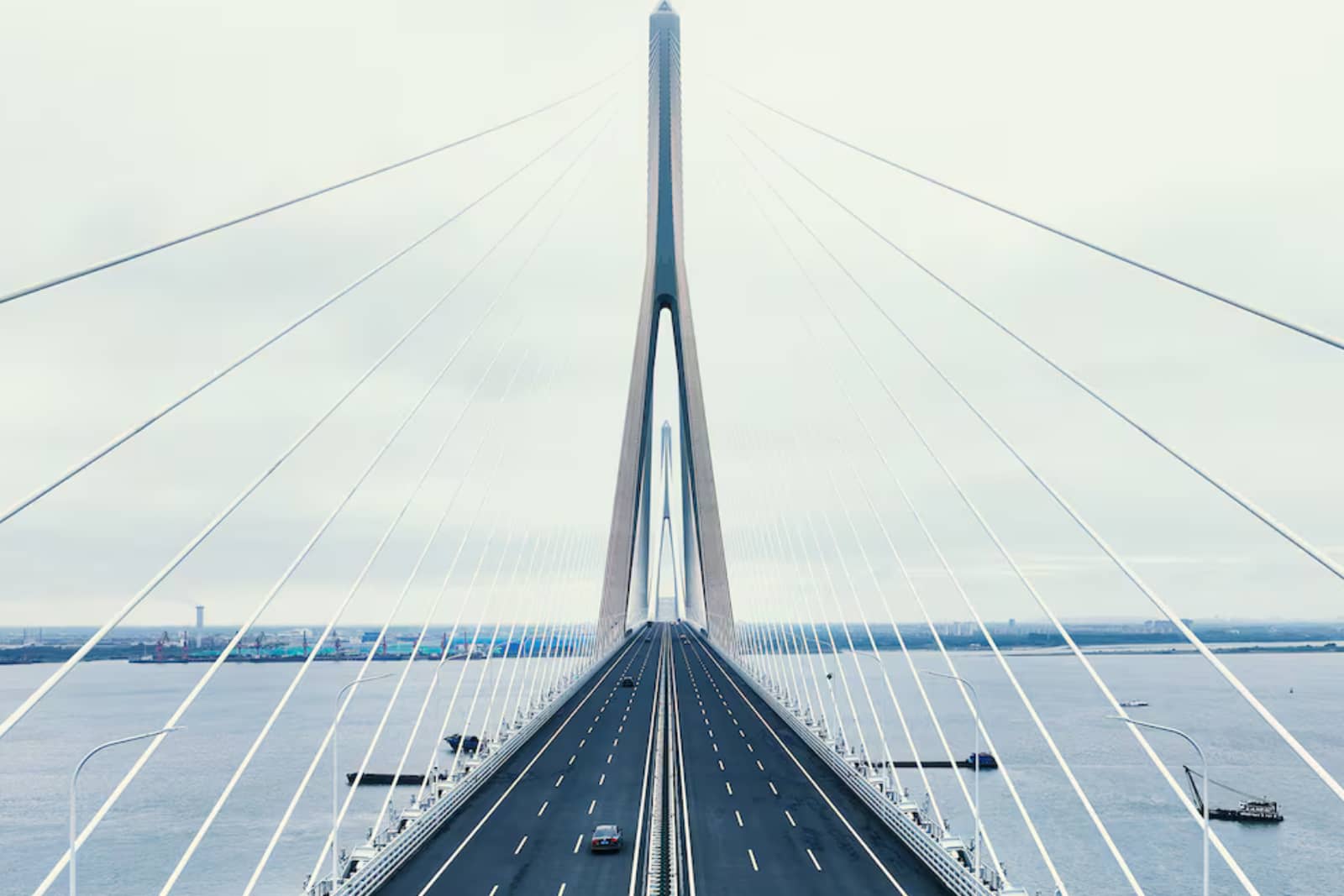 Puente moderno con cables sobre un río, carretera despejada, cielos nublados